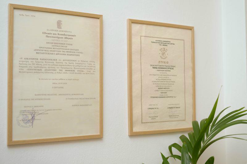 Δύο κορνιζαρισμένα πτυχία στον τοίχο του γραφείου.